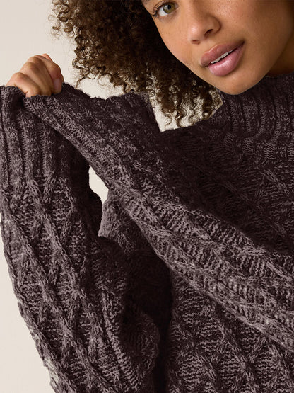 A person wearing a dark brown Eileen Fisher Peruvian Cotton Boucle Fluff Turtleneck in Coffee, pulling up one sleeve of the cable-knit sweater.