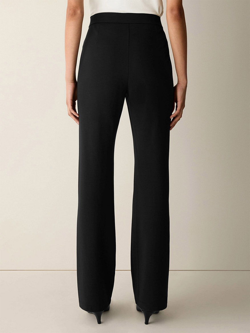 A person wearing the Eileen Fisher Extra-Fine Ponte Kick Pant in Black, featuring a high-waisted, straight-leg silhouette crafted from ultra-light ponte fabric, paired with black heeled shoes and photographed from the back against a plain background.