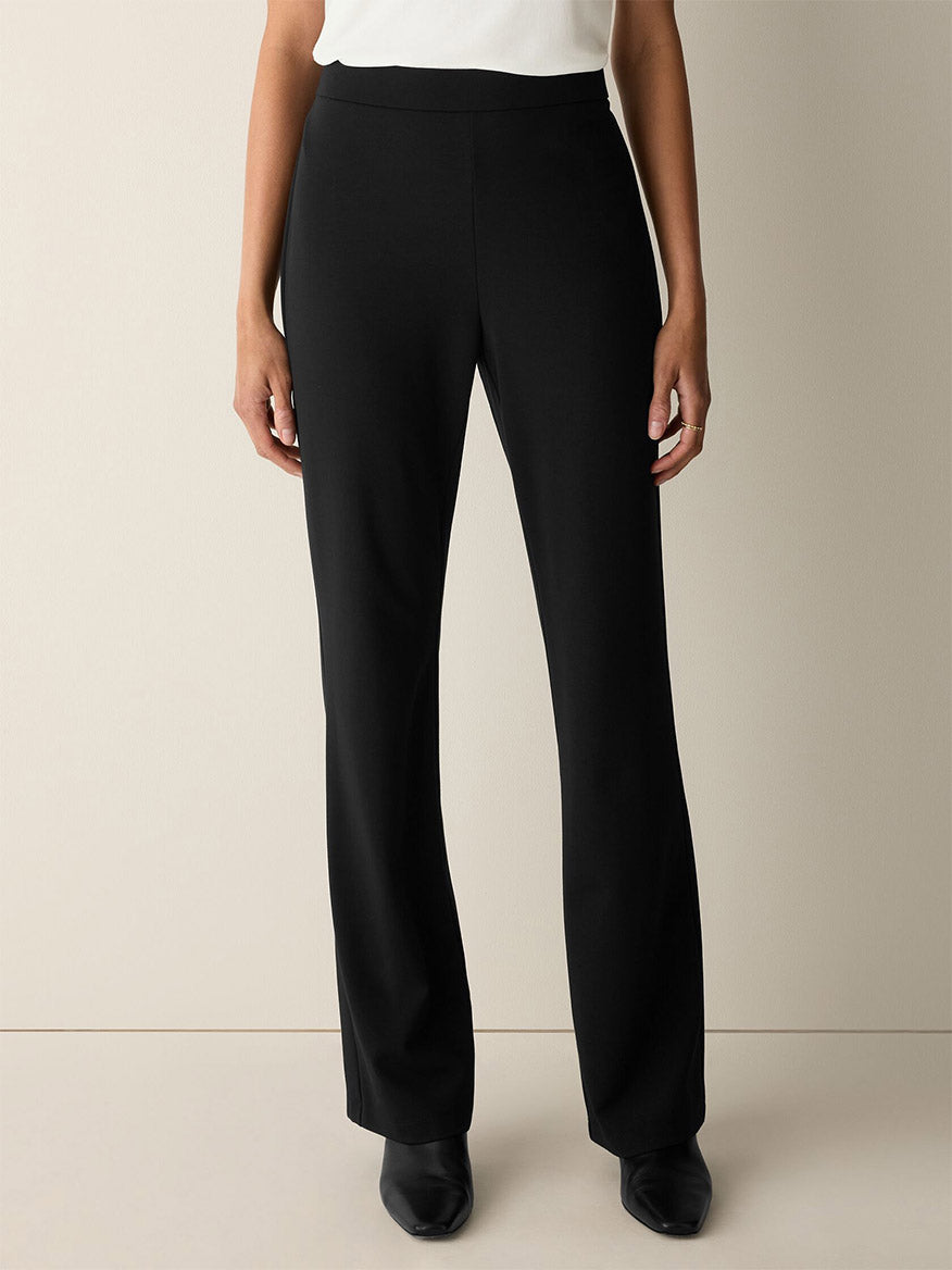 Person standing against a neutral background, wearing the Eileen Fisher Extra-Fine Ponte Kick Pant in Black, crafted from the lightest ponte fabric, paired with black shoes. Their hands are relaxed at their sides. Upper body is partially visible and the top appears white.