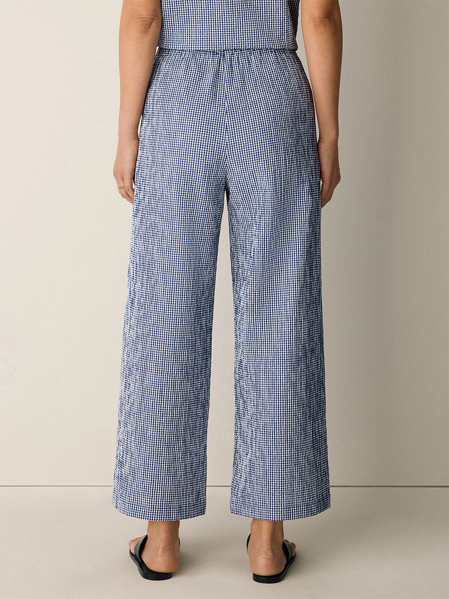 A person stands with their back to the camera, wearing Eileen Fisher Organic Cotton Pucker Check Wide-Leg Pant in Light Dive and black sandals against a plain background.