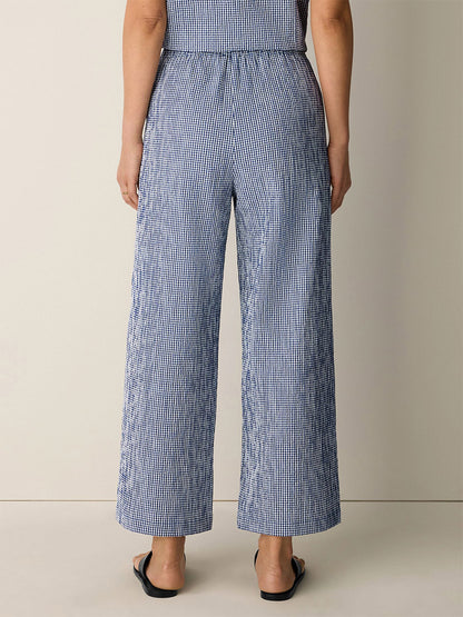 A person stands with their back to the camera, wearing Eileen Fisher Organic Cotton Pucker Check Wide-Leg Pant in Light Dive and black sandals against a plain background.