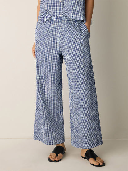 A person wearing the Eileen Fisher Organic Cotton Pucker Check Wide-Leg Pant in Light Dive and black sandals stands against a plain light background with hands in pockets.