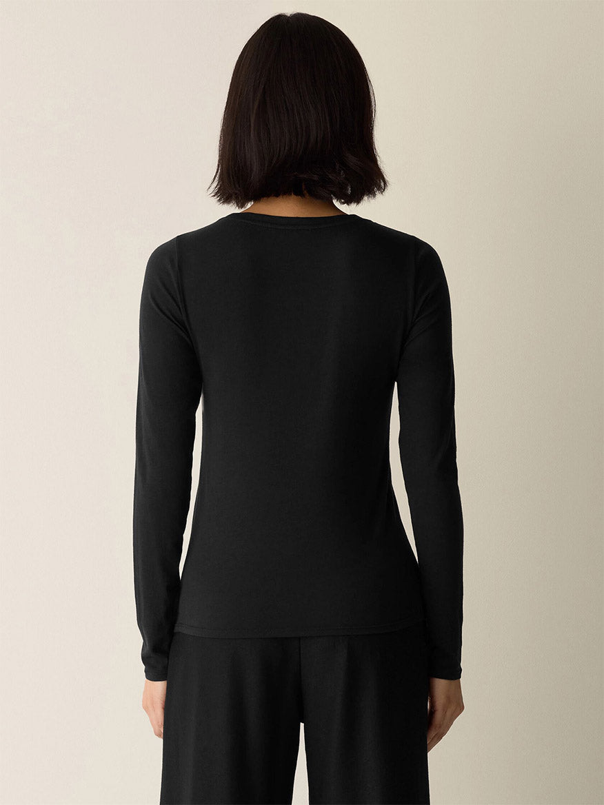 A person with short dark hair is shown from behind, wearing the Eileen Fisher Sheer Cotton Blend Knit Round Neck Tee in Black and black pants against a neutral background.