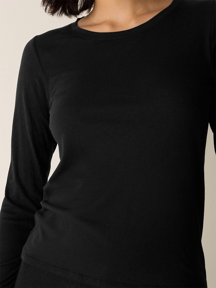 Someone wearing the Eileen Fisher Sheer Cotton Blend Knit Round Neck Tee in Black, shown from shoulders to waist against a neutral background.