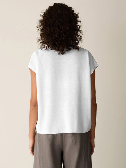Viewed from behind, a person with curly hair wears the Eileen Fisher Organic Linen Cotton V-Neck Top in white and gray pants, standing against a plain light-colored background.