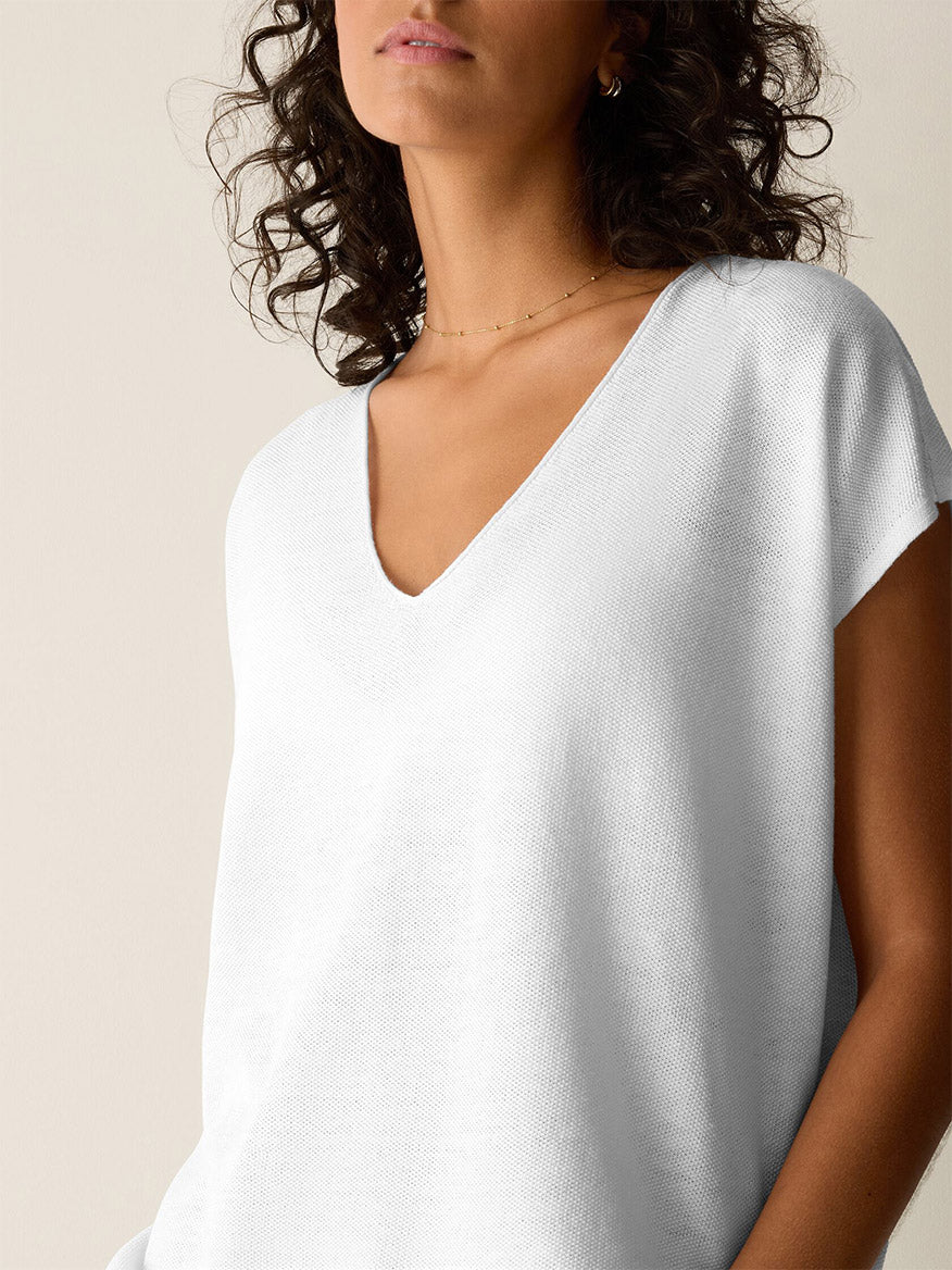 Woman with curly hair wears the Eileen Fisher Organic Linen Cotton V-Neck Top in White, styled with minimal jewelry and set against a neutral background.