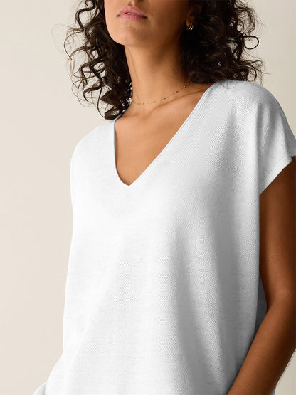 Woman with curly hair wears the Eileen Fisher Organic Linen Cotton V-Neck Top in White, styled with minimal jewelry and set against a neutral background.