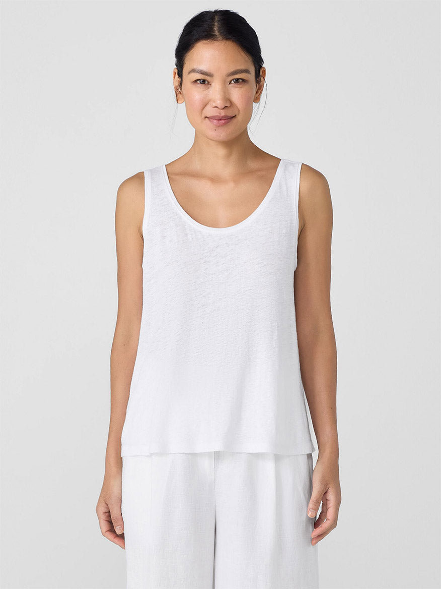 A woman wears the Eileen Fisher Organic Linen Jersey Scoop Neck Tank in White with white pants, standing against a plain light background.