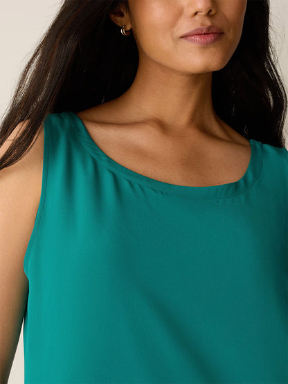 A woman wearing the Eileen Fisher Silk Crepe de Chine Easy Dress in teal; image shows her from shoulders to just above the chest, with part of her face visible.