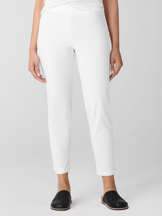 A person wearing Eileen Fisher Washable Stretch Crepe Pant in white with black slip-on shoes stands against a neutral background.