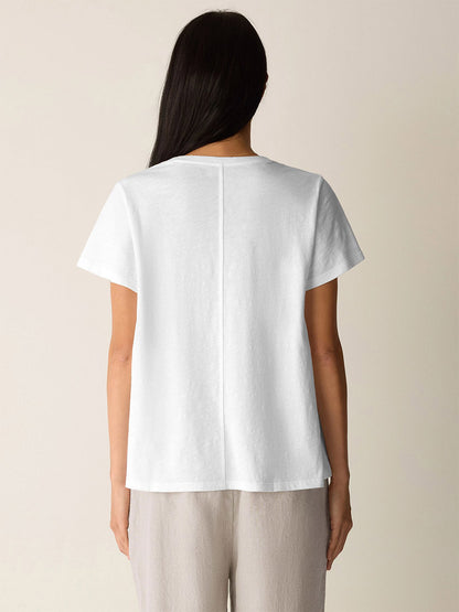 Person stands with their back to the camera, wearing an Eileen Fisher Organic Cotton Slubby Jersey Crew Neck Tee in White and light-colored pants, set against a neutral background.