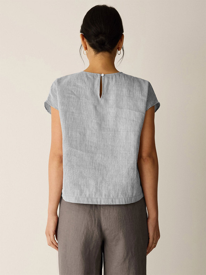 Person standing with their back to the camera, wearing the Eileen Fisher Striped Linen Sheen Square Top in Wheat and loose dark gray pants against a plain light background.