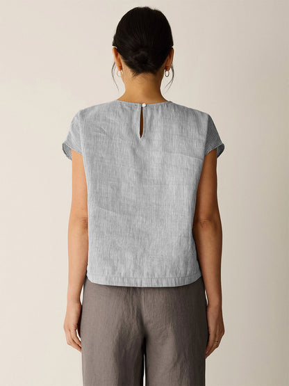 Person standing with their back to the camera, wearing the Eileen Fisher Striped Linen Sheen Square Top in Wheat and loose dark gray pants against a plain light background.