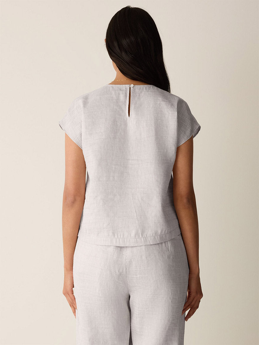 A person stands with their back to the camera, wearing the Eileen Fisher Striped Linen Sheen Square Top in Wheat and matching pants.