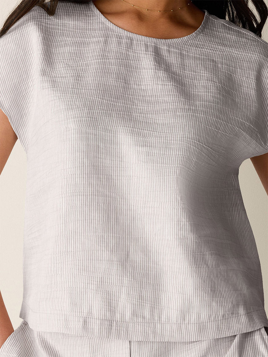 A person wearing the Eileen Fisher Striped Linen Sheen Square Top in Wheat, a short-sleeved, light-colored, subtly striped organic linen top with a boxy fit, shown from shoulders to waist.