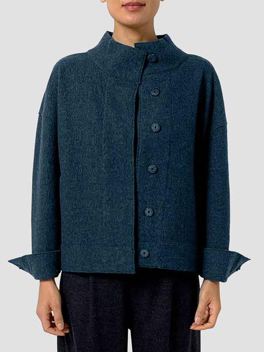 Someone wears the Eileen Fisher Lightweight Boiled Wool Stand Collar Jacket in Alpine, which features a dark blue hue, stand collar, boxy fit, and long sleeves, paired with black pants against a plain light background.