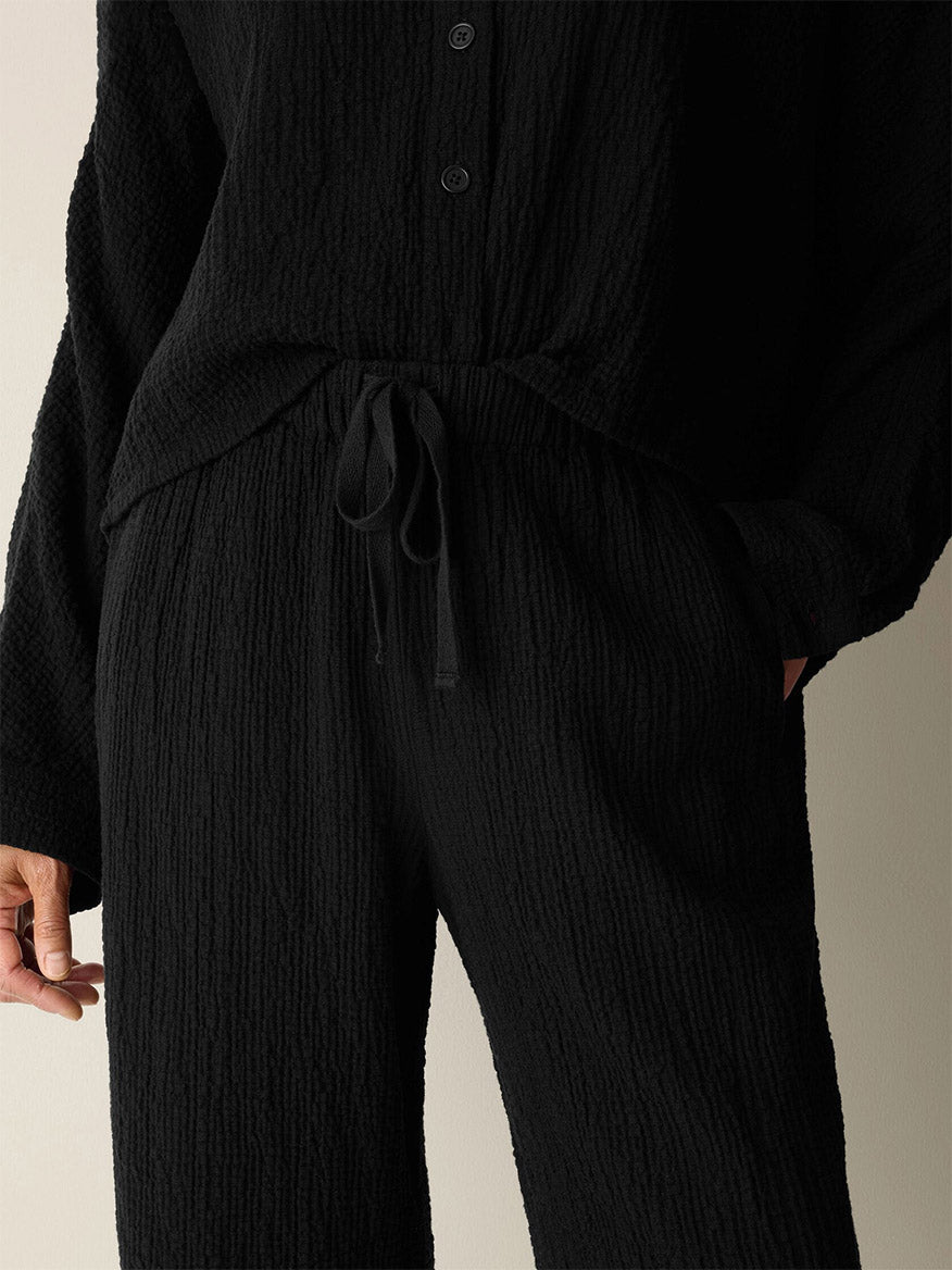 Person wearing an Eileen Fisher Organic Cotton Doubleweave Straight Pant in Black, styled with a textured black button-up top, one hand in a pocket, shown from shoulders to knees against a neutral background.