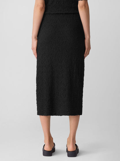 A person faces away, wearing the Eileen Fisher Bubble Jacquard Pencil Skirt in Black with black shoes against a plain background.