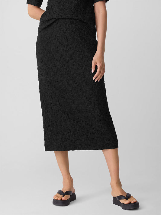 A person wearing an Eileen Fisher Bubble Jacquard Pencil Skirt in Black and black sandals stands against a plain light-colored background.