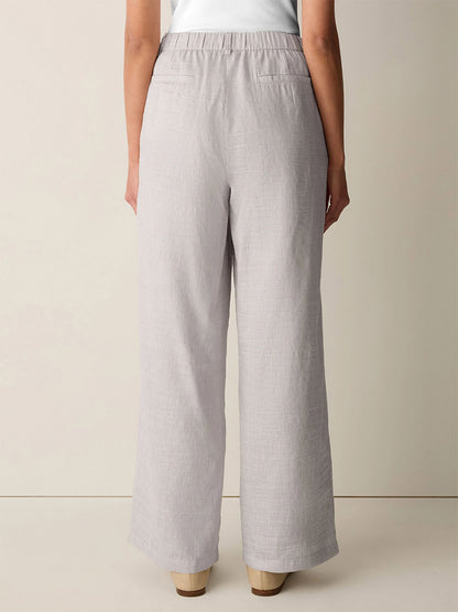 A person stands facing away, wearing the Eileen Fisher Striped Linen Sheen Full-Length Trouser in Wheat with beige shoes and a classic collar jacket against a neutral background.