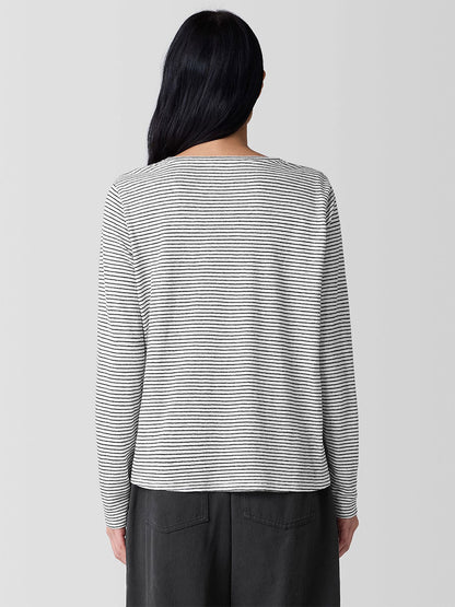 A long-haired person wears an Eileen Fisher Striped Organic Linen Jersey Long-Sleeve Tee in White/Black, paired with dark pants, facing away.