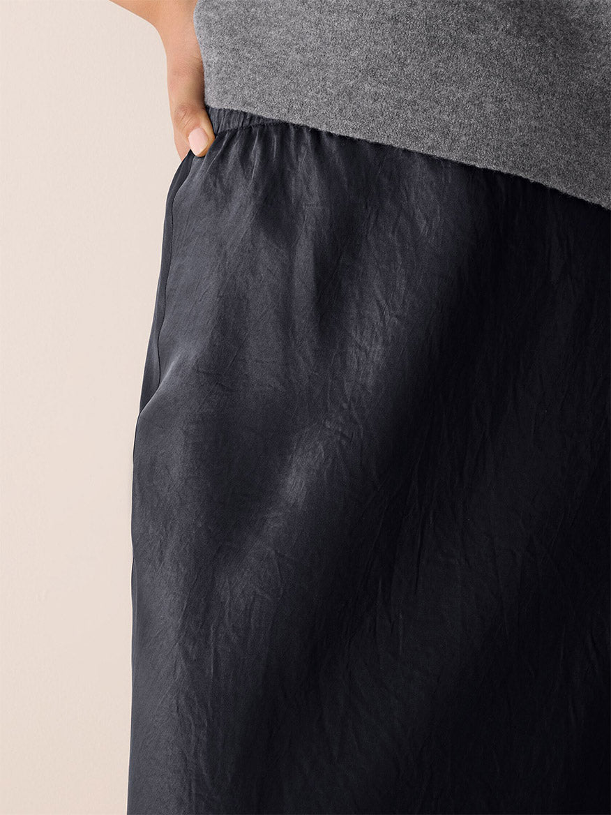 A person wearing a grey top and the Eileen Fisher Textured Satin Slip Skirt in Graphite, with their hand in the skirt pocket.
