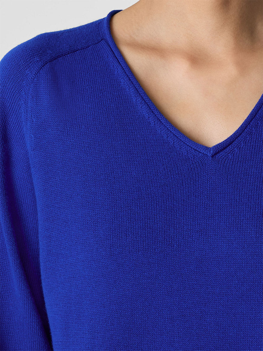 Close-up of a person in an Eileen Fisher Peruvian Cotton Blend V-Neck Top in Lapis, highlighting the collar and upper chest against a plain, light-colored background.