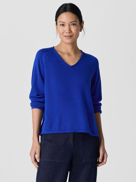 A person in an Eileen Fisher Peruvian Cotton Blend V-Neck Top in Lapis paired with dark pants stands against a plain background, showcasing sustainable Tencel Lyocell.