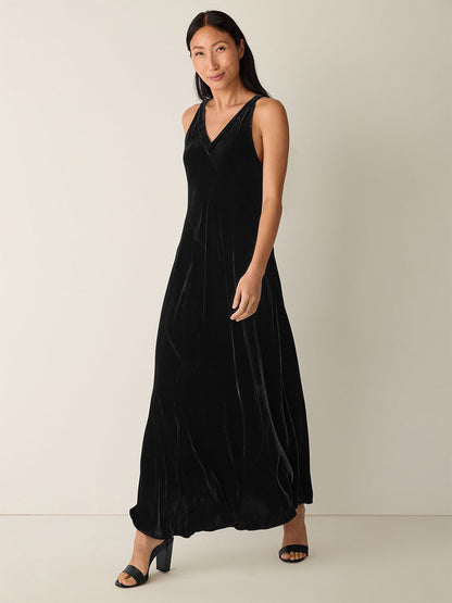 A woman stands against a plain background wearing the Eileen Fisher Velvet V-Neck Dress in Black and black heeled sandals.