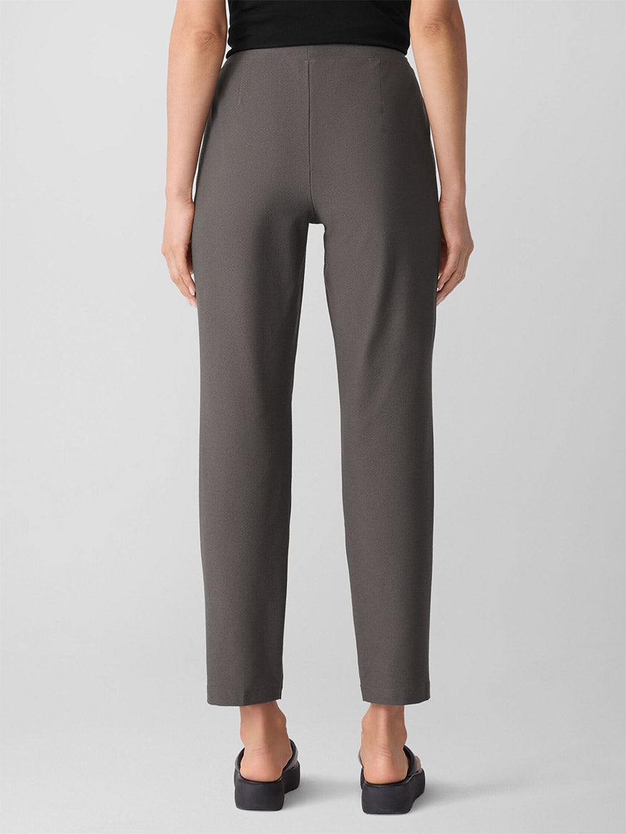 A person is seen from the back wearing Eileen Fisher Washable Stretch Crepe Pant in Rye with black shoes, against a plain light background.