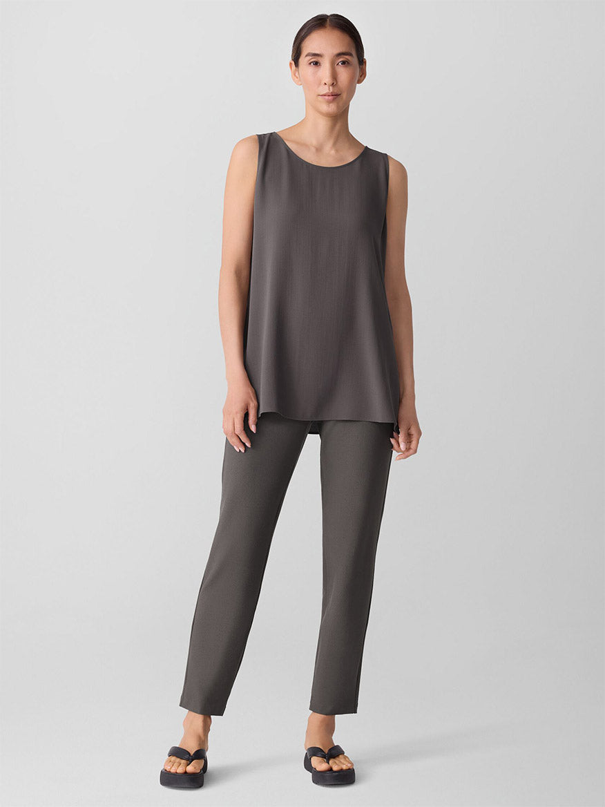 A woman stands against a plain background wearing an Eileen Fisher loose, sleeveless taupe top, black sandals, and the Eileen Fisher Washable Stretch Crepe Pant in Rye.