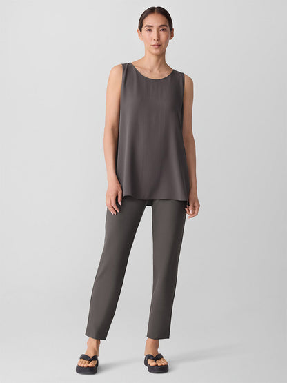 A woman stands against a plain background wearing an Eileen Fisher loose, sleeveless taupe top, black sandals, and the Eileen Fisher Washable Stretch Crepe Pant in Rye.