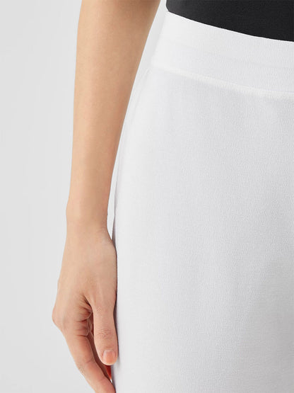 Close-up of a person wearing a white skirt and a black top, focusing on the left hand resting against the side of the skirt, reminiscent of Eileen Fisher Washable Stretch Crepe Pant in White.