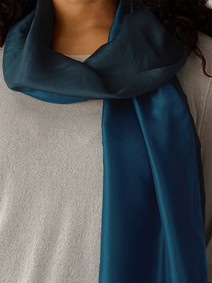A person wearing the Eileen Fisher Watercolor Organic Silk Scarf in Sailor Blue, draped over a light gray textured top.