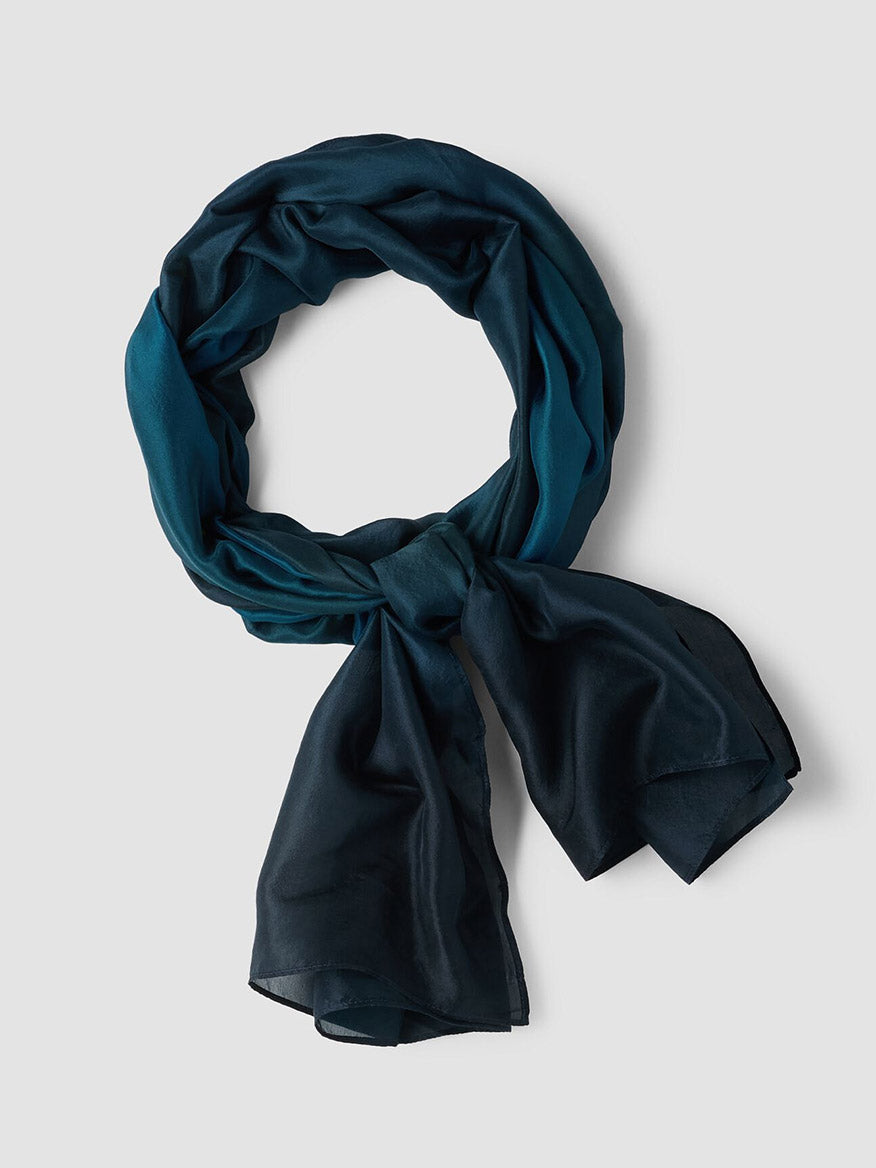 An Eileen Fisher Watercolor Organic Silk Scarf in Sailor Blue, featuring a lightweight and Fair Trade design, is displayed in a circular shape with a loose knot on a plain light grey background.