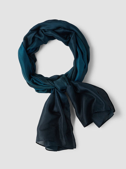 An Eileen Fisher Watercolor Organic Silk Scarf in Sailor Blue, featuring a lightweight and Fair Trade design, is displayed in a circular shape with a loose knot on a plain light grey background.