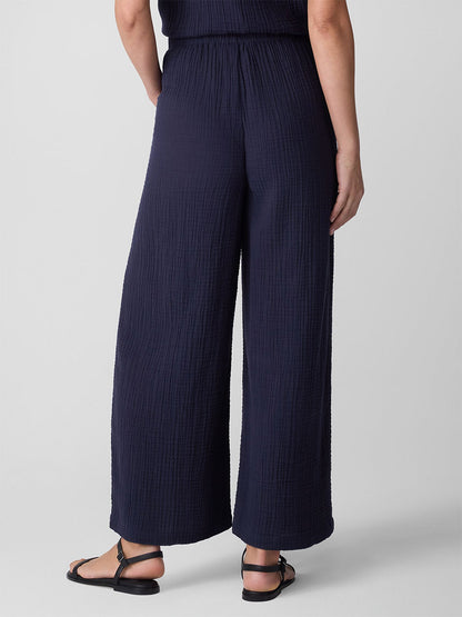 Wearing the Eileen Fisher Organic Cotton Lofty Gauze Wide-Leg Pant in Ink, styled with black sandals, a person stands against a plain light background, shown from the back.