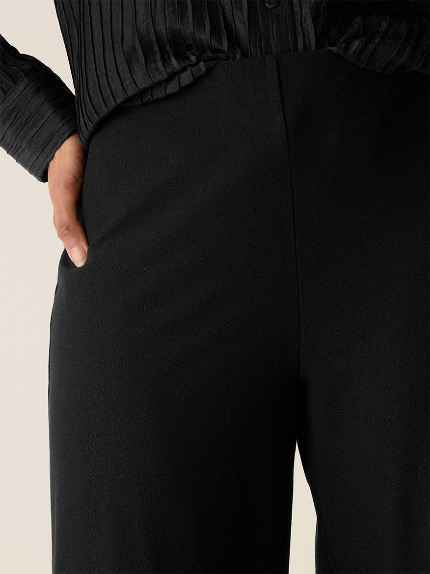 A person wears the Eileen Fisher Washable Stretch Crepe Wide-Leg Pant in Black with one hand in their pocket, photographed from the waist down.