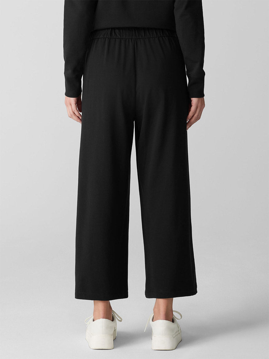 A person stands facing away, wearing the Eileen Fisher Pima Cotton Stretch Jersey Wide-Leg Pant in Black with a matching long-sleeve top and white sneakers against a plain background.