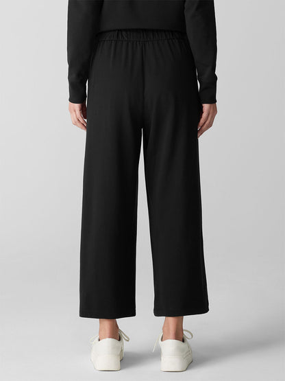 A person stands facing away, wearing the Eileen Fisher Pima Cotton Stretch Jersey Wide-Leg Pant in Black with a matching long-sleeve top and white sneakers against a plain background.