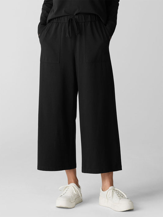 A person wearing Eileen Fisher Pima Cotton Stretch Jersey Wide-Leg Pant in Black with patch pockets and a drawstring waist, styled with white sneakers.