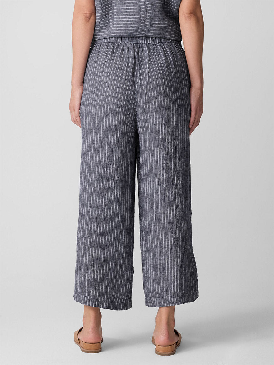 Person stands with their back to the camera wearing Eileen Fisher Puckered Organic Linen Wide-Leg Pant in Black/White and tan sandals against a plain light background.
