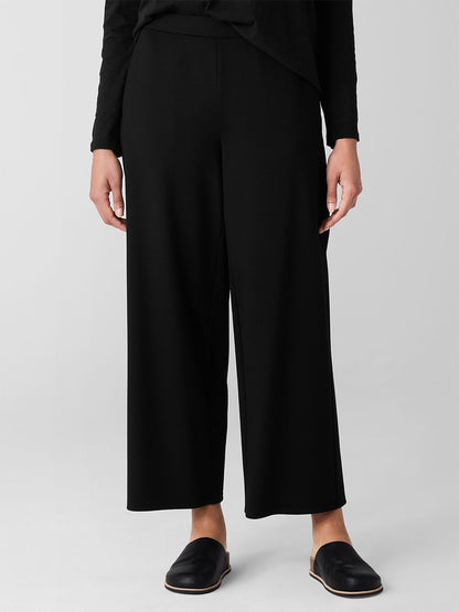 A person stands against a plain background wearing Eileen Fisher Washable Flex Ponte Wide-Leg Pants and black shoes. The high-waisted design adds elegance, and being Fair Trade Certified ensures ethical production.