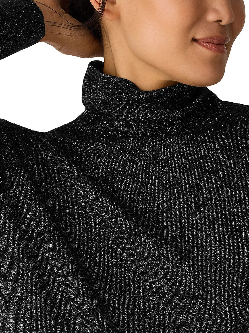 Close-up of a woman in the Eileen Fisher Wool Lurex Turtleneck Sweater in Black, featuring metallic fibers, her face partially visible and left arm raised.