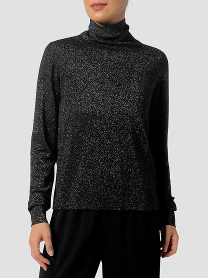 Model wears the Eileen Fisher Wool Lurex Turtleneck Sweater in Black, featuring subtle metallic shimmer, paired with black pants against a plain light gray background.