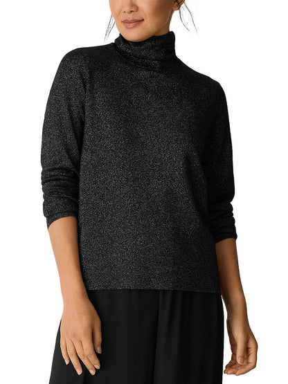 A person wearing the Eileen Fisher Wool Lurex Turtleneck Sweater in Black with black pants, standing against a white background.