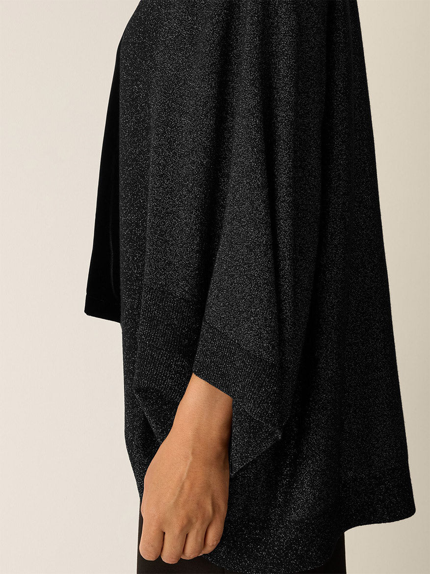 A person wearing the Eileen Fisher Wool Shimmer Serape in Black—featuring a loose fit, wide sleeves, and regenerative fiber—shown from the side against a plain background.
