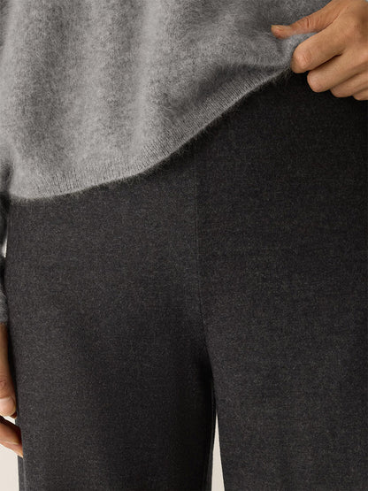 Close-up of a person wearing a light grey regenerative wool sweater and Eileen Fisher Mélange Boiled Wool Jersey Wide-Leg Pant in Charcoal, with one hand visible near the edge of the sweater.