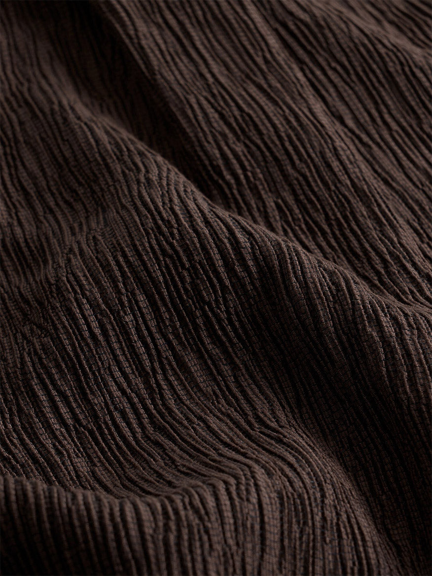 Close-up of the Eileen Fisher Woven Plissé V-Neck Dress in Truffle, showcasing its dark brown, textured plissé fabric with a crinkled, ribbed surface and visible diagonal folds across the material.