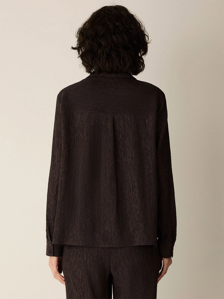 Person with short, curly dark hair wearing the Eileen Fisher Woven Plissé Classic Collar Shirt in Truffle, facing away from the camera against a plain light background.